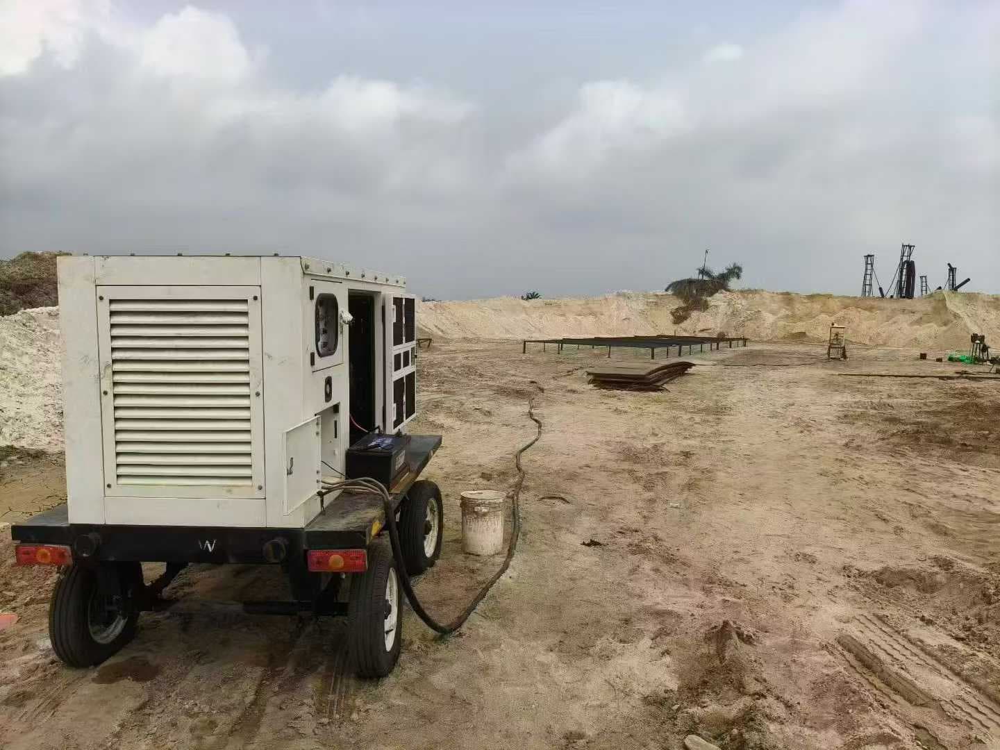 A white silent canopy set on a two-wheel trailer standing on sand at a yard, connected by a power cable