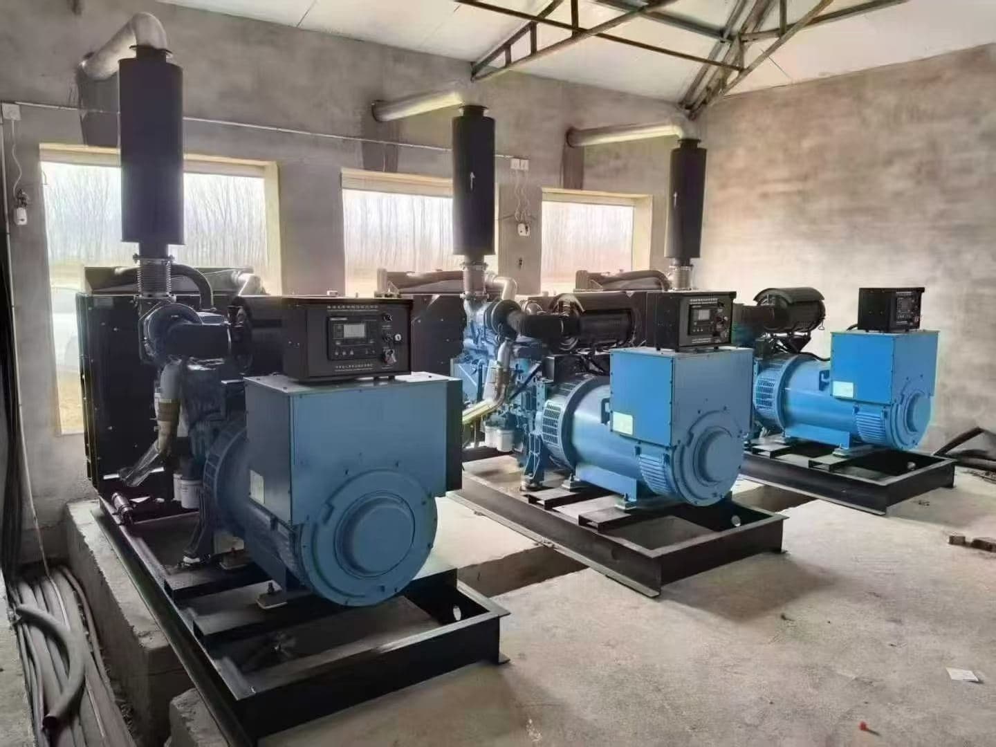 Three open-type sets in a row inside a raw concrete building, each with an exhaust silencer ducted up through the ceiling